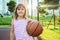 Portrait of a little girl with a basketball ball on an outdoor playground, on a sunny summer day