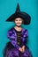 Portrait of little girl in black hat and witch clothing. Halloween. Fairy. Tale. Studio portrait on blue background