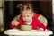 Portrait of little girl blowing on hot porridge to cool sitting in feeding chair