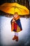 Portrait of Little girl in blue coat, yellow scarf and umbrella in winter, spring or autumn day in nature in the