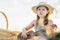 Portrait of little girl in hat sitting on blanket in dry hay field, having picnic, learning playing ukulele. Side view