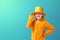 Portrait of a little girl in a knitted mustard jacket and a shiny yellow cylinder hat of a magician on a turquoise background.