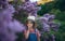 Portrait of a little girl in nature blooming lilac-purple meadow, putting her finger into nose.