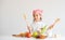 Portrait of little girl smile and holds wood ladle and fork in front of vegetables and fruits with concept of little chef on white
