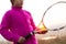 Portrait of little girl is training skill, outside of tennis court, in field at sunset. Wearing pink sweater.