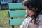 portrait of a little long-haired modest girl sitting on a green bench outdoors
