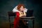 Portrait of little red-headed girl in image of royal person with laptop isolated over dark green background. Studying