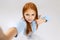 Portrait of little redhaired Caucasian girl, child posing, taking selfie isolated over white studio background.