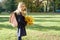 Portrait of little schoolgirl with yellow maple leaves school bag, on sunny autumn day, copy space