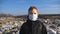 Portrait of little serious boy in medical protective mask stands against the background of dirty garbage dump and looks