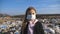 Portrait of little serious girl in medical protective mask stands against the background of dirty garbage dump and looks