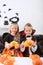 portrait of little siblings in halloween costumes sitting on sofa at table with pumpkins