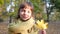 Portrait of little smiling girl with yellow leaf in her hands in autumn park