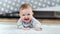 Portrait of little smiling toddler lying on fluffy carpet looking at camera in modern interior