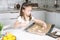 Portrait of little studiously kid girl, sitting chair kitchen, making different easter shape dough cookies, dripping pan