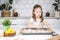 Portrait of little studiously kid girl, sitting chair kitchen, making different easter shape dough cookies, dripping pan