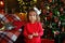Portrait of a little surprised girl in a festively decorated room with lights of garlands for Christmas. A child in red pajamas