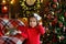 Portrait of a little surprised girl in a festively decorated room with lights of garlands for Christmas. A child in red pajamas