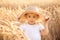Portrait of little toddler child in straw hat standing in wheat field among golden spikes holding loaf of bread. Summer in country