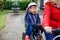 Portrait of little toddler girl with security helmet on the head sitting in bike seat and her mother with bicycle. Safe