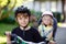 Portrait of little toddler girl with security helmet sitting in bike seat of brother. Kid boy on bicycle with lovely