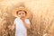 Portrait of little toddler in straw hat eating bread standing at wheat field among golden spikes in summer day at countryside