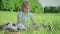 Portrait of lonely Caucasian little boy sitting on green sunny meadow with soccer ball and using tablet. Portrait of sad