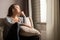 Portrait of lonely sad Ñaucasian young woman sitting near window of apartments.