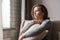 Portrait of lonely sad Ñaucasian young woman sitting near window and hugs pillow.