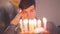 Portrait lonely sad boy sitting in front of little cake with lighted candles looking on it. Unhappy man has birthday