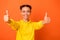 Portrait of lovely youth showing thumbs up smiling wear hoodie jumper isolated over orange background