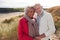 Portrait of Loving Senior Couple Standing And Hugging On Walk In Sand Dunes On Winter Beach Vacation