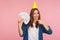 Portrait of lucky charming rich girl in checkered shirt and party cone on head smiling and pointing at money