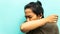 A portrait of a Malay man coughing and sneezing to his elbow neck with closing both eyes on isolated blue background