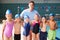 Portrait Of Male Coach With Children In Swimming Class Standing Edge Of Indoor Pool