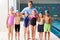 Portrait Of Male Coach With Children In Swimming Class Standing Edge Of Indoor Pool