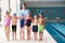 Portrait Of Male Coach With Children In Swimming Class Standing Edge Of Indoor Pool