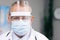 Portrait of male Doctor in Glasses Wearing a Transparent Protective Face Shield, Mask and Overalls in a Hospital Room at