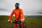 Portrait of a male downhill cyclist in a full face helmet and goggles with an orange windbreaker jacket with a raincoat