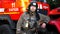 Portrait of male firefighter in helmet and balaclava standing near a big red car. Young fireman in full equipment