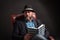 Portrait of man with beard and hat sitting on leather chair reading book.