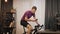 Portrait of man cyclist is training on exercise bicycle in front of laptop computer with smartphone in hands. Indoor cycling. Spor