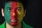 Portrait of a man with the flag of the Cameroon painted on his face on black background.