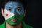 Portrait of a man with the flag of the Djibouti painted on his face on black background.
