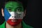 Portrait of a man with the flag of the Equatorial Guinea painted on his face on black background.
