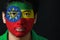 Portrait of a man with the flag of the Ethiopia painted on his face on black background.