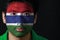 Portrait of a man with the flag of the Gambia painted on his face on black background.