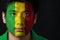 Portrait of a man with the flag of the Mali painted on his face on black background.