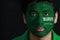 Portrait of a man with the flag of the Saudi Arabia painted on his face on black background.