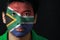 Portrait of a man with the flag of the South Africa painted on his face on black background.